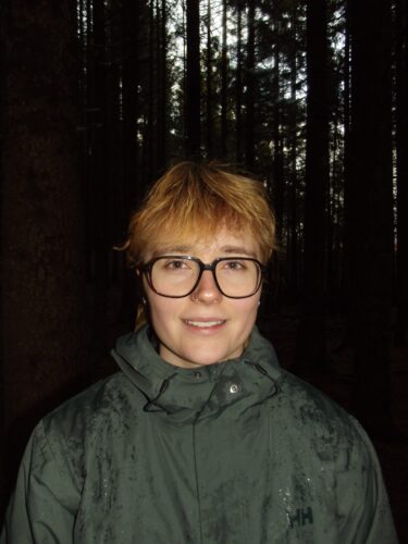 Bild på Ella som ler i en skogsmiljö.